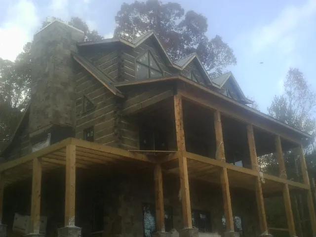 Stone chimney and dormers on a large log home with a timber porch in Monticello